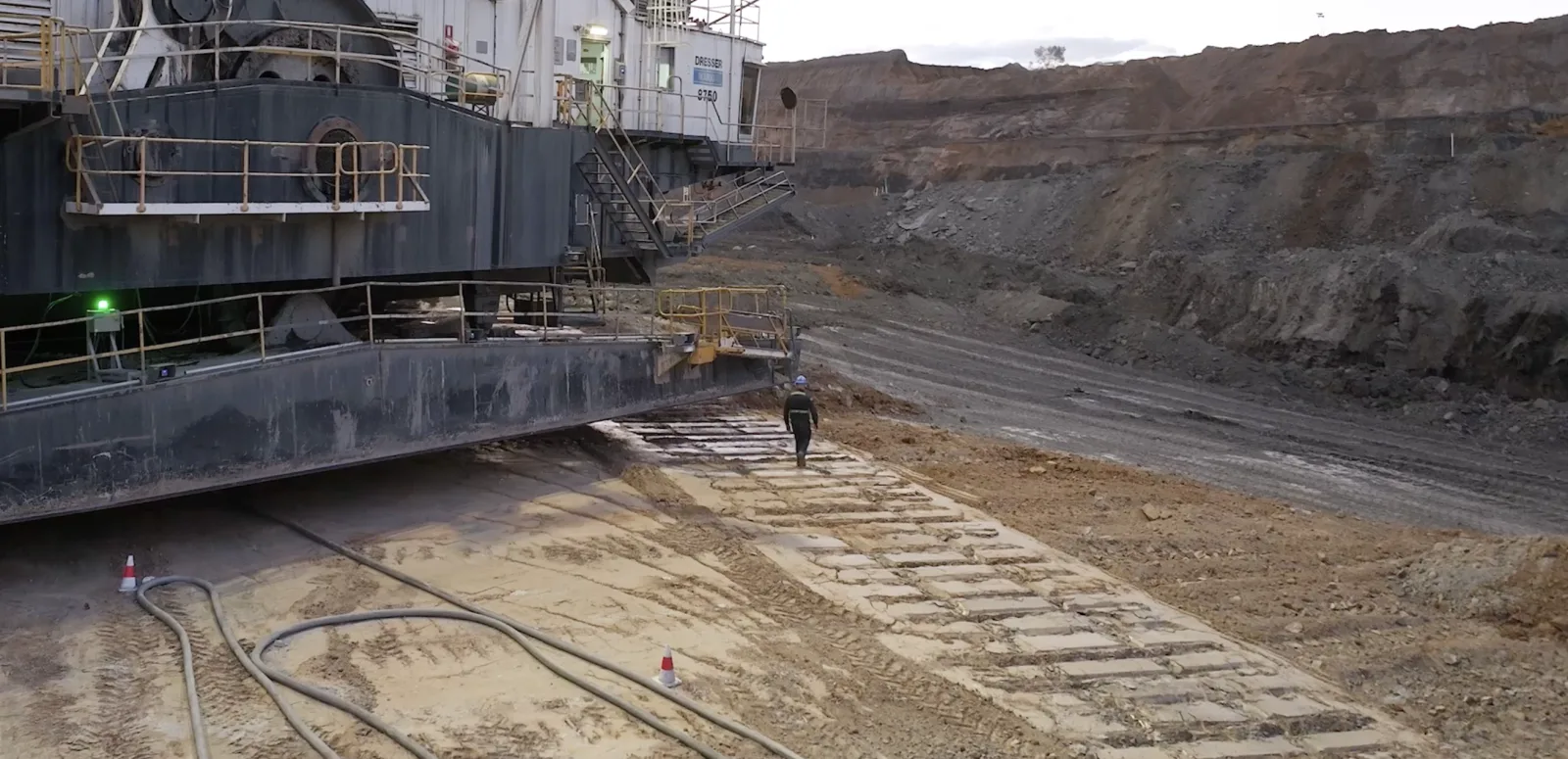 Illustration: a person on foot beside a working dragline&rsquo;s tub, inside the stop zone drawn on the ground, and the machine brought to a controlled stop